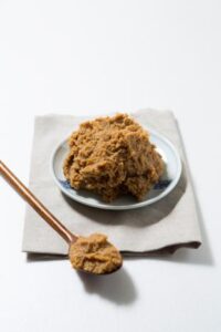 Brown Doenjang paste on a white plate, and a wooden spoonful